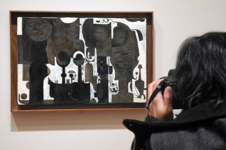 A visitor takes a photo of the painting 'The Mosque' by Sudanese artist Ibrahim El-Salahi at the Museum of Modern Art (MoMA) in New York, US, 6 February 2017. The museum demonstrates against the travel ban imposed by US-President Donald Trump by exhibiting works by artists from the affected countries. Photo: Johannes Schmitt-Tegge/dpa | usage worldwide (Photo by Johannes Schmitt-Tegge/picture alliance via Getty Images)