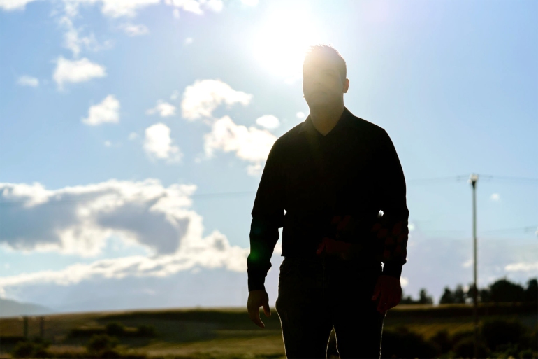 Front view of man standing with his eyes closed dressed in black on a sunny day.. gettyimages-1472184268