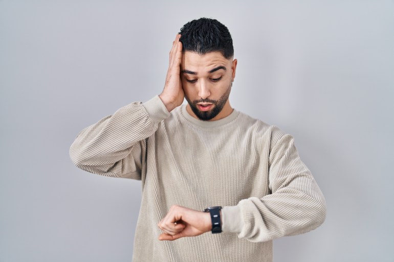 Young handsome man standing over isolated background looking at the watch time worried, afraid of getting late