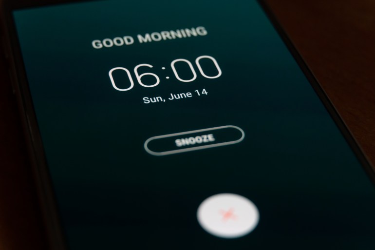 On a black smartphone, an alarm clock rings for 6 am with the inscription Good morning close-up, background