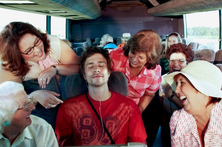 People on coach, women around man with eyes closed wearing headphones - stock photo