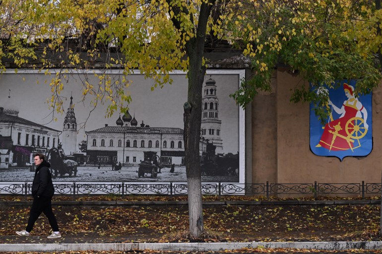 A young man walks past a wall decorated with the city's coat of arms featuring a spinner in Ivanovo, a city located some 250 km northeast of Moscow, on October 20, 2023. - From the shelves of the library, the old lady grabs books whose place she naturally knows. Orwell, Sorokin, Dostoevsky. Authors who, for her, help to pierce the darkness of contemporary Russia. (Photo by Natalia KOLESNIKOVA / AFP)