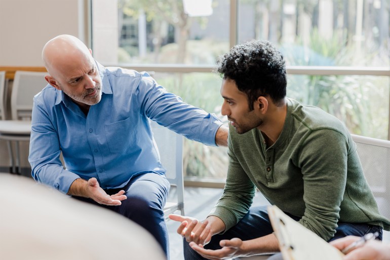 The empathetic mature adult man gestures and asks questions as he helps the younger man work through his problems.