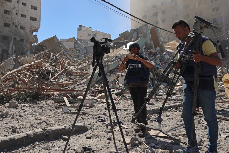 Journalists stand next to the rubble of Jala Tower, which was housing international press offices, following an Israeli airstrike in the Gaza Strip on May 15, 2021. An Israeli air strike demolished the 13-floor building housing Qatar-based Al-Jazeera television and American news agency The Associated Press in the Gaza Strip. (Photo by MOHAMMED ABED / AFP)