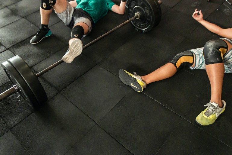 Two Men Lying on Gym Floor Beside Black Barbell