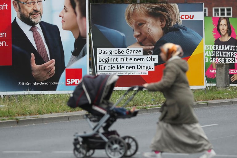 صورة تظهر سيدة مسلمة بالقرب من لافتات قديمة الحزب عليها صورة ميركل Political Parties Campaign In Federal Elections BERLIN, GERMANY - SEPTEMBER 08: A Muslim woman pushes a pram past election campaign billboards that show German Social Democrat (SPD) chancellor candidate Martin Schulz (L), German Chancellor and Christian Democrat (CDU) Angela Merkel (C) and Greens Party co-lead candidate Katrin Goering-Eckardt on September 8, 2017 in Berlin, Germany. Germany will hold federal elections on September 24. Merkel is seeking a fourth term and currently holds an approximate 14-point lead over her main rival, Schulz. Both the German Greens Party and the Free Democrats (FDP) are hoping to position themselves to be part of the next coalition government. The right-wing, populist Alternative for Germany (AfD) will likely finish above the 5% election votes minimum and hence win seats in the Bundestag. (Photo by Sean Gallup/Getty Images)