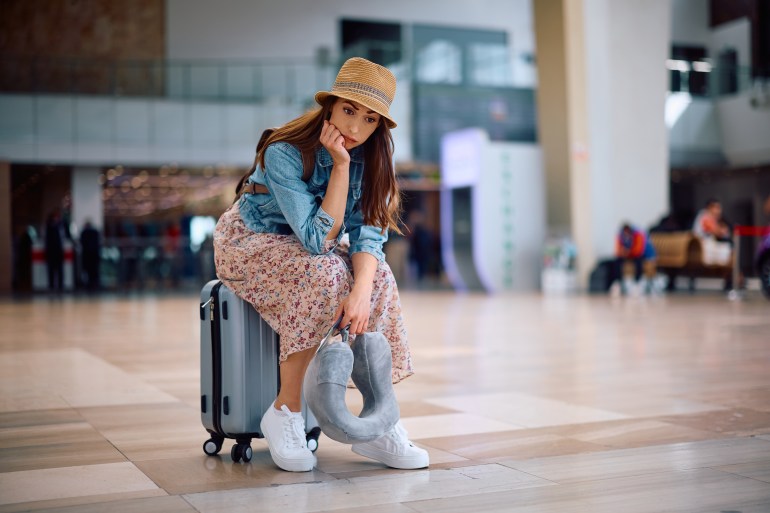 Young worried woman sitting on her suitcase at the airport. Copy space.