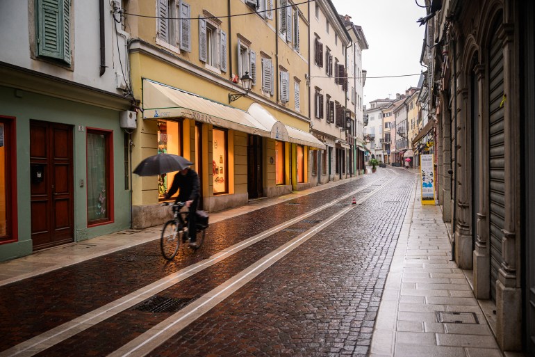 A cyclist rides, holding an umbrella, on the Via Rastello alley in Gorizia, Italy on January 23, 2025. Film director Anja Medved has long dwelled on the pain of her grandmum, who was separated from her family when the border between Italy and then Yugoslavia was drawn up after World War II in 1947. Since then, the barbed wire has disappeared as the European Union and then Schengen abolished controls, and this year the European Capital of Culture, for the first time a cross-border event, brings together Gorizia and its younger twin Nova Gorica. (Photo by Jure Makovec / AFP)