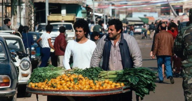 Two vendors selling oranges and vegetables from a cart walk through the Shatila refugee camp on January 13, 1984 [Peter Charlesworth/LightRocket via Getty Images]